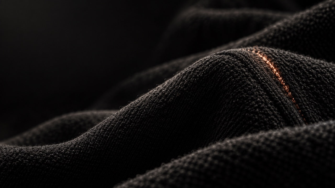 Close view of black looped knit fabric lit from the side, with a single copper stitch running along a fold.