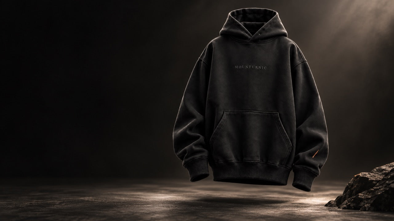 A black oversized hoodie suspended in darkness above a stone floor, lit from the upper right.